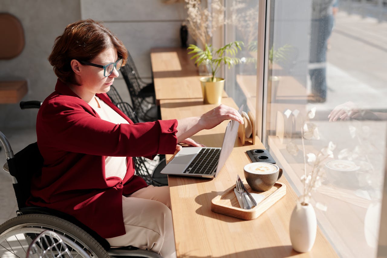 why-choose-us Woman in wheelchair working on a laptop in a bright café, showcasing remote work lifestyle.