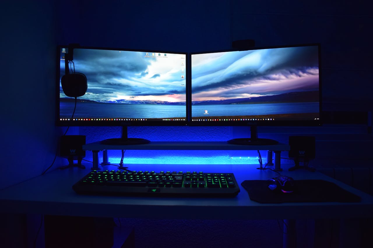 about-bg Dual monitors with blue lighting on a gaming desk setup.